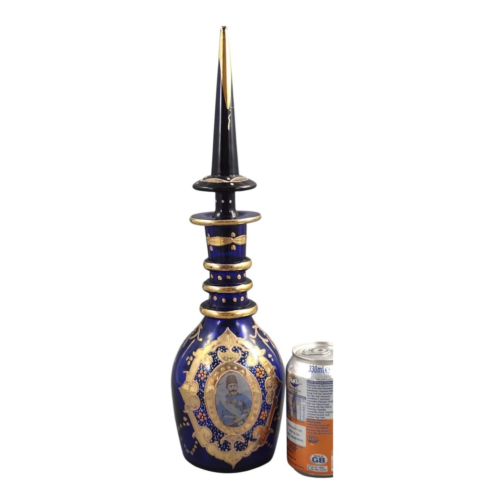 A cobalt blue Bohemian glass decanter decorated with elaborate gold enamelling and a painted portrait medallion, featuring a tall pointed stopper. View V