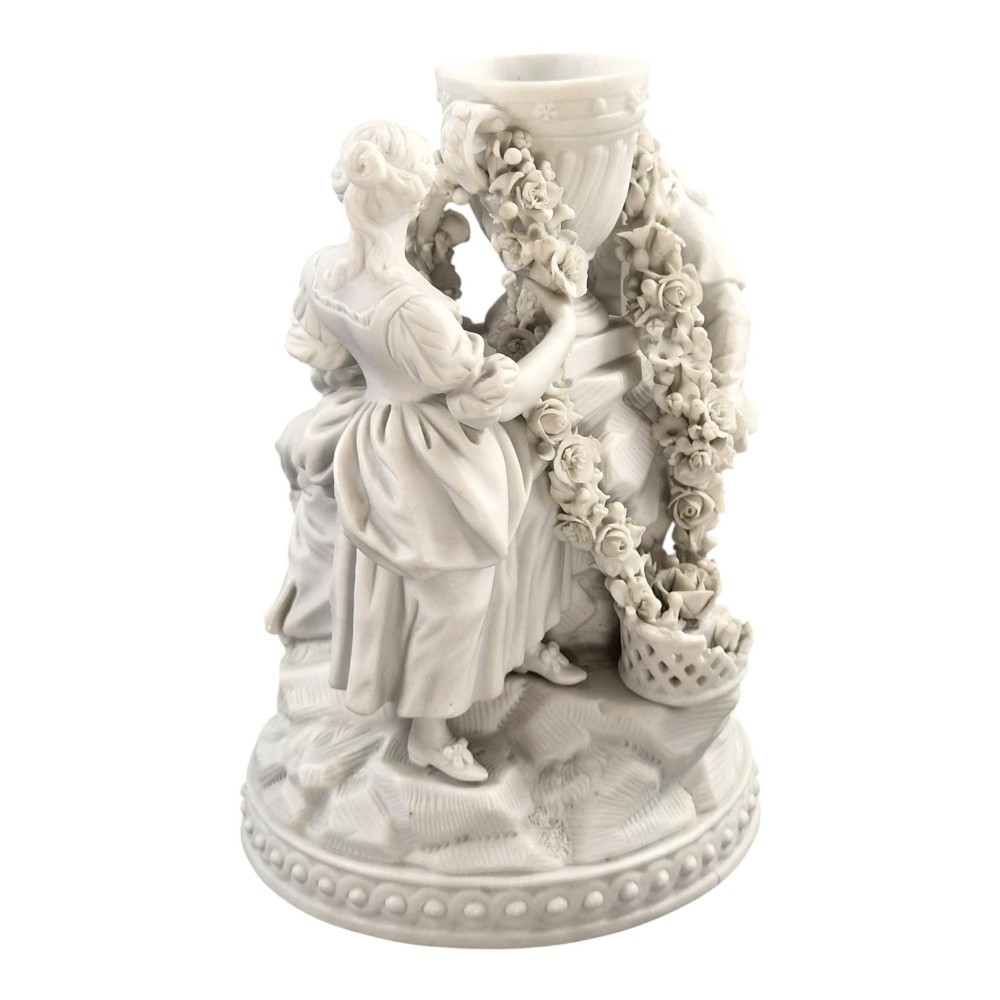 A white matte biscuit porcelain sculptural group depicting three figures and a central urn adorned with delicate floral garlands on a decorative circular base. View V
