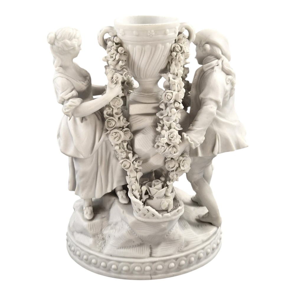 A white matte biscuit porcelain sculptural group depicting three figures and a central urn adorned with delicate floral garlands on a decorative circular base. View VI