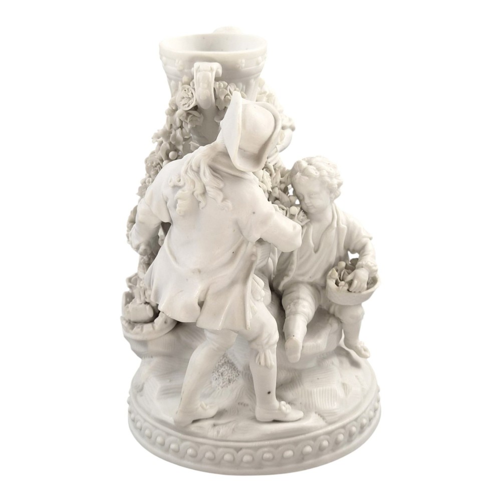 A white matte biscuit porcelain sculptural group depicting three figures and a central urn adorned with delicate floral garlands on a decorative circular base. View VIII
