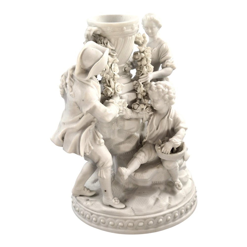 A white matte biscuit porcelain sculptural group depicting three figures and a central urn adorned with delicate floral garlands on a decorative circular base. View IX