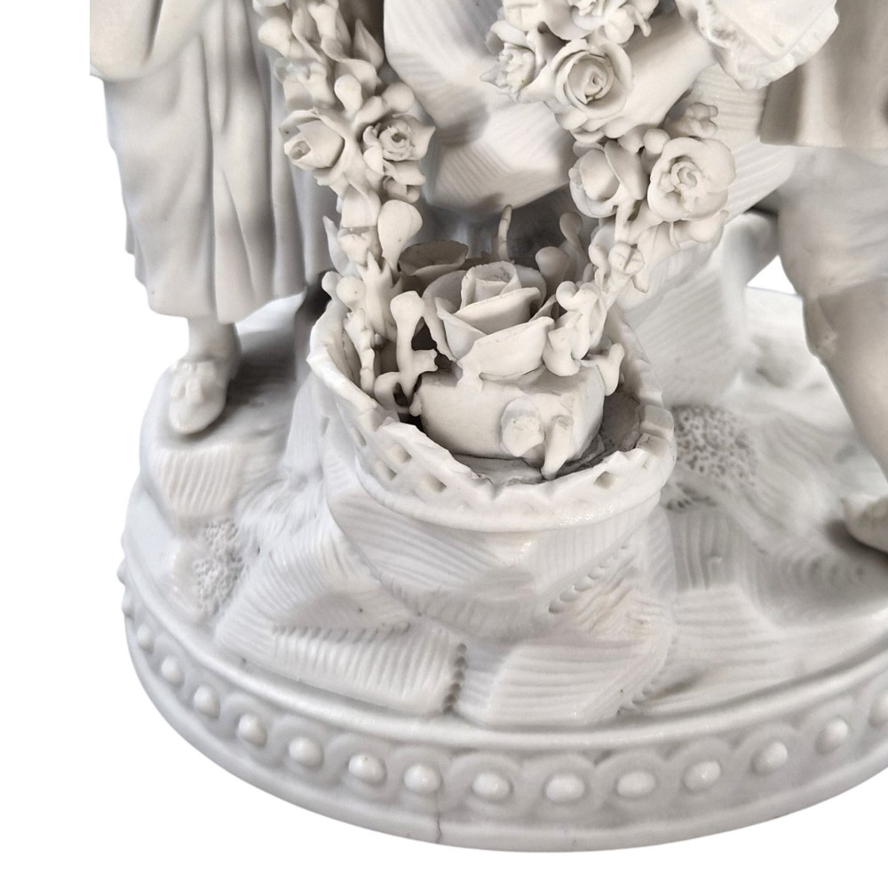 A white matte biscuit porcelain sculptural group depicting three figures and a central urn adorned with delicate floral garlands on a decorative circular base. View XI