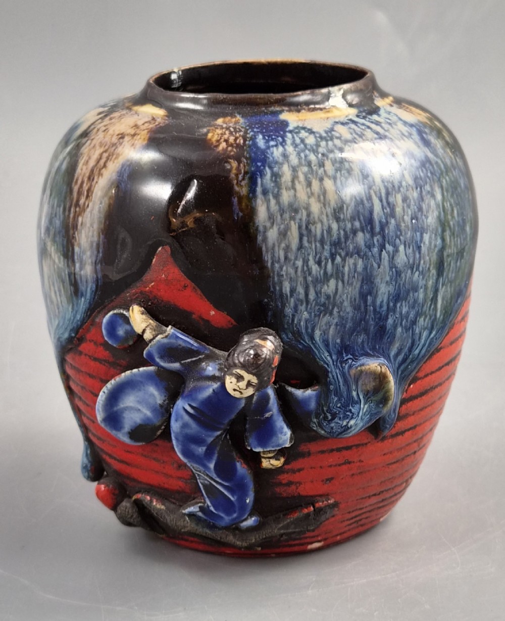 A rounded Japanese Sumida Gawa ceramic jar featuring heavy blue flambe dripping glaze over a ribbed red body with an applied relief climbing figure.