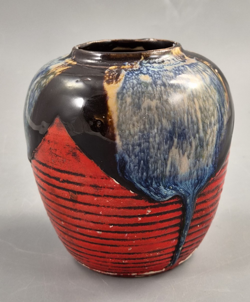 A rounded Japanese Sumida Gawa ceramic jar featuring heavy blue flambe dripping glaze over a ribbed red body with an applied relief climbing figure. View III