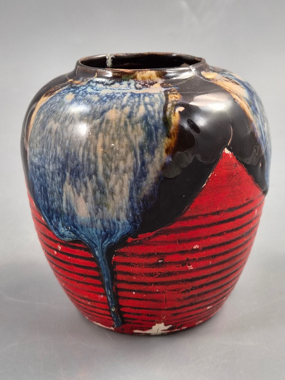 A rounded Japanese Sumida Gawa ceramic jar featuring heavy blue flambe dripping glaze over a ribbed red body with an applied relief climbing figure. View IV