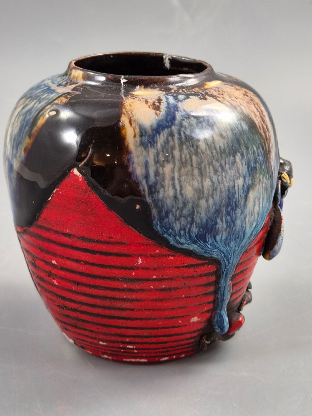 A rounded Japanese Sumida Gawa ceramic jar featuring heavy blue flambe dripping glaze over a ribbed red body with an applied relief climbing figure. View V