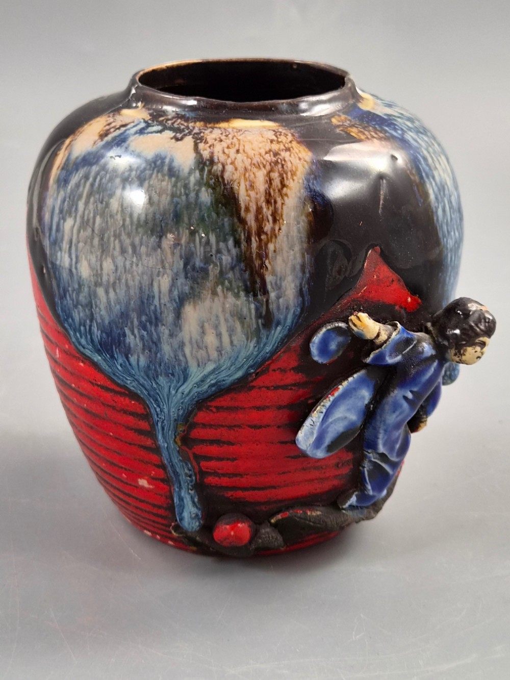 A rounded Japanese Sumida Gawa ceramic jar featuring heavy blue flambe dripping glaze over a ribbed red body with an applied relief climbing figure. View VI
