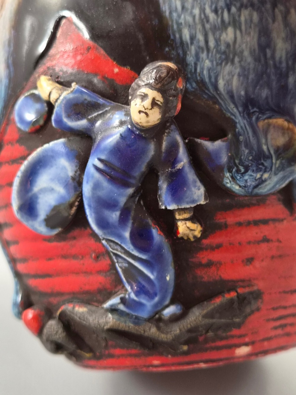 A rounded Japanese Sumida Gawa ceramic jar featuring heavy blue flambe dripping glaze over a ribbed red body with an applied relief climbing figure. View VIII