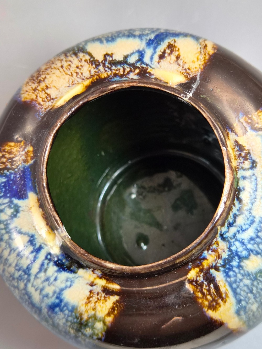 A rounded Japanese Sumida Gawa ceramic jar featuring heavy blue flambe dripping glaze over a ribbed red body with an applied relief climbing figure. View X