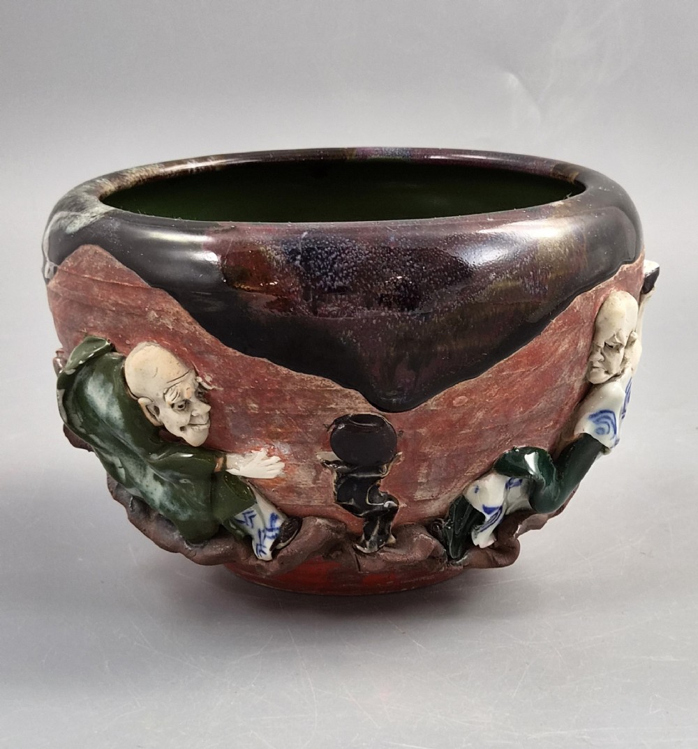 An antique Japanese Sumida Gawa ceramic bowl featuring heavy dark flambe glaze over a red terracotta body adorned with three-dimensional applied figures in relief.