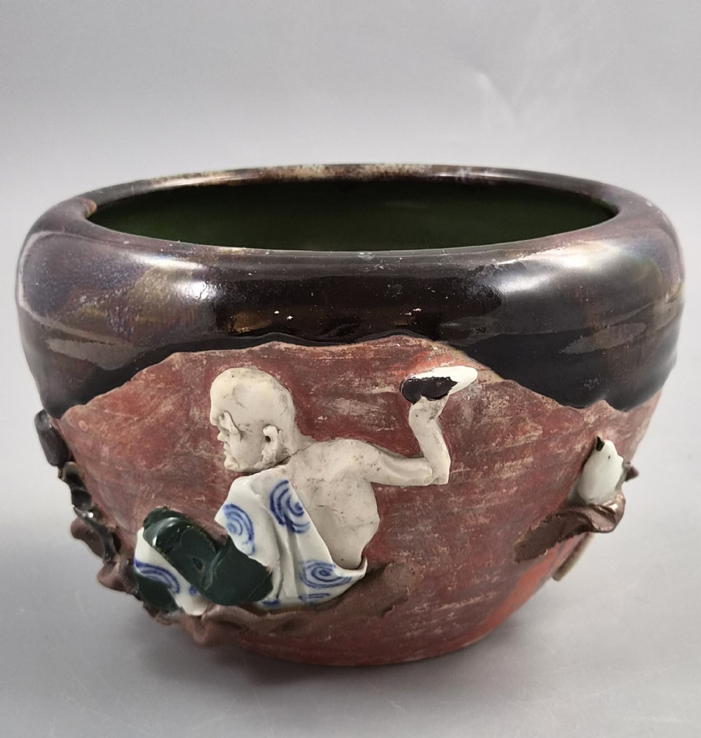 An antique Japanese Sumida Gawa ceramic bowl featuring heavy dark flambe glaze over a red terracotta body adorned with three-dimensional applied figures in relief. View II