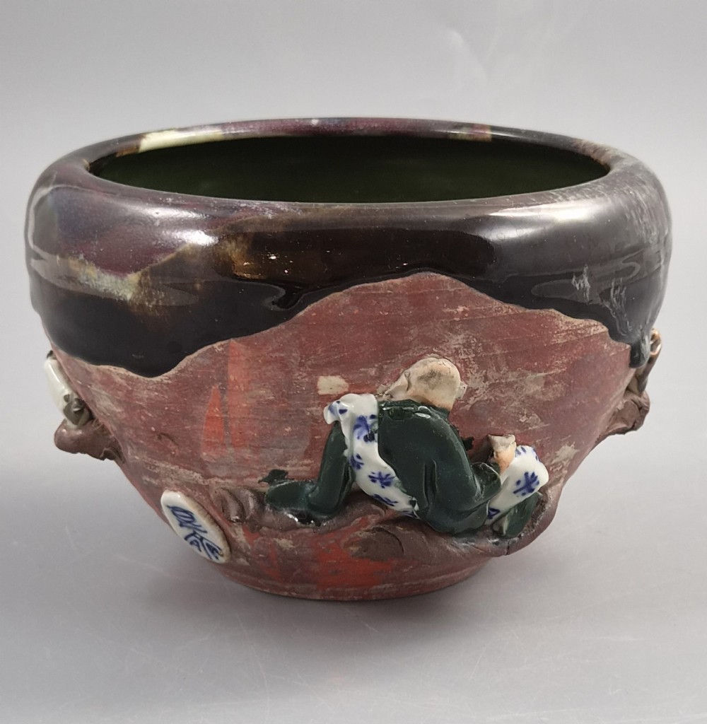An antique Japanese Sumida Gawa ceramic bowl featuring heavy dark flambe glaze over a red terracotta body adorned with three-dimensional applied figures in relief. View IV