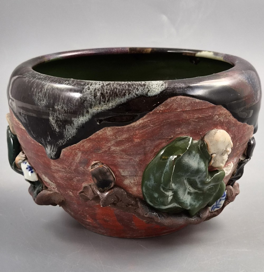 An antique Japanese Sumida Gawa ceramic bowl featuring heavy dark flambe glaze over a red terracotta body adorned with three-dimensional applied figures in relief. View VI