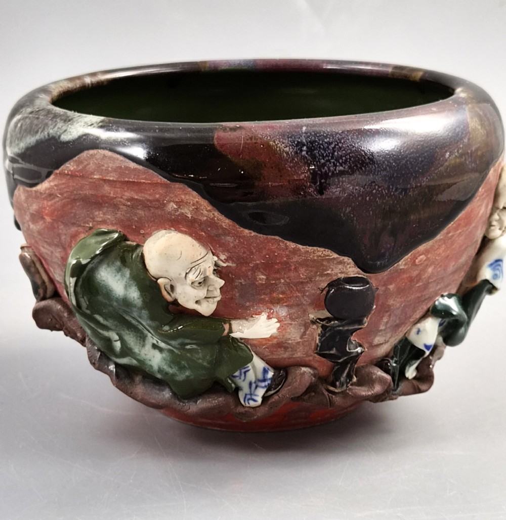 An antique Japanese Sumida Gawa ceramic bowl featuring heavy dark flambe glaze over a red terracotta body adorned with three-dimensional applied figures in relief. View VII