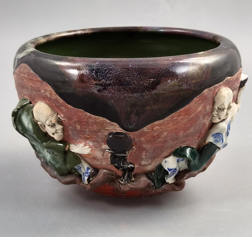 An antique Japanese Sumida Gawa ceramic bowl featuring heavy dark flambe glaze over a red terracotta body adorned with three-dimensional applied figures in relief. View VIII