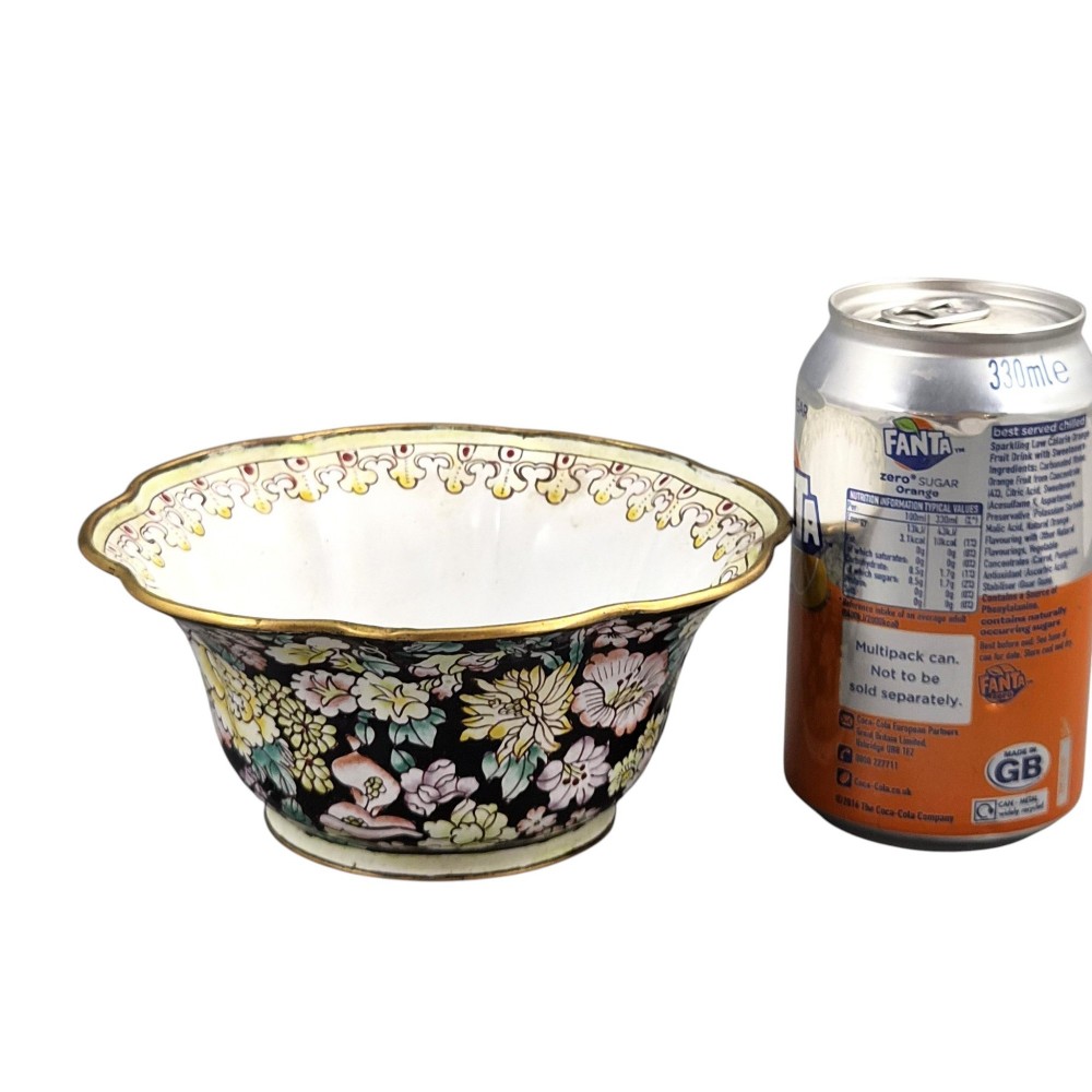 A Chinese Canton enamel-on-copper bowl featuring a lobed rim, a black ground exterior decorated with colourful floral motifs, and a white interior with a patterned border. View IX