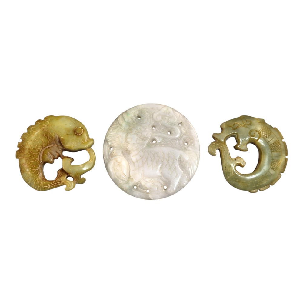 A group of three carved Chinese stone amulets featuring a carp, a central circular bi disc with a qilin, and a chilong dragon.