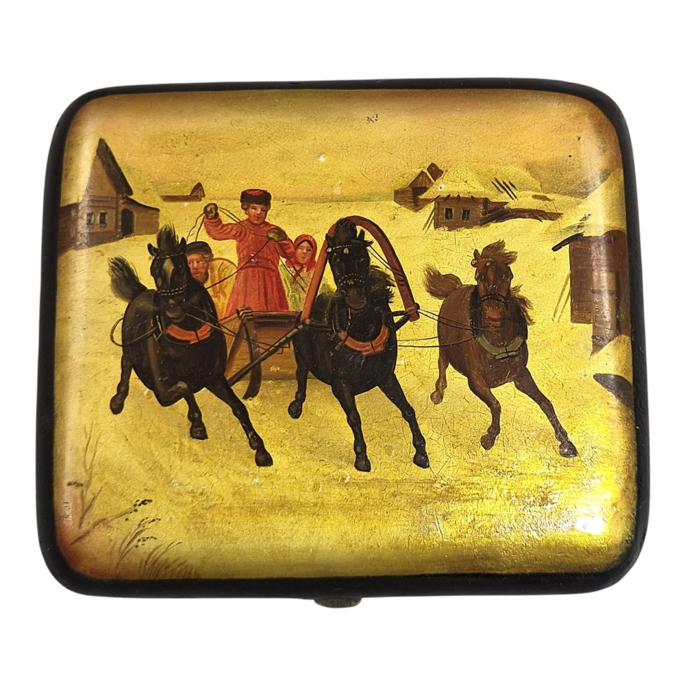 A rectangular 19th-century Russian lacquer cigarette case featuring a hand-painted scene of three horses pulling a sleigh across a snowy landscape on a gold background.