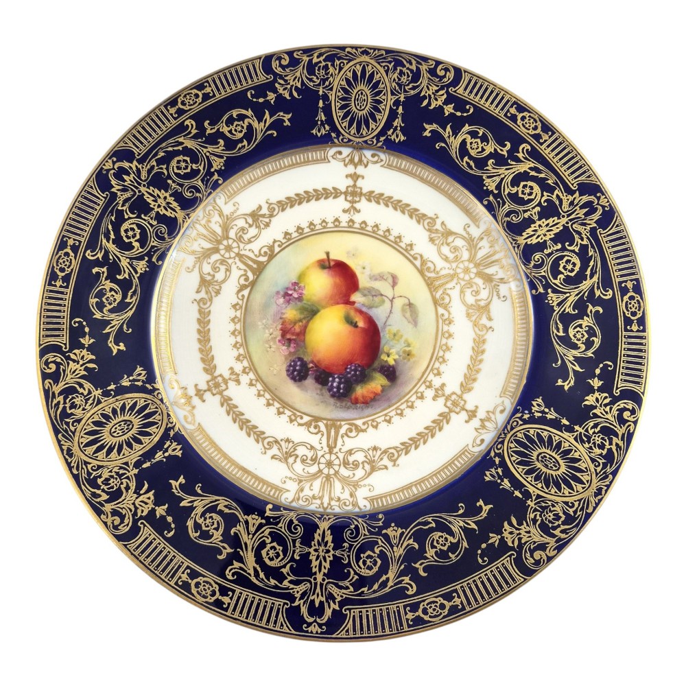 A circular Royal Worcester porcelain cabinet plate featuring a cobalt blue rim with detailed gold gilding framing a central painted still life of apples and berries.