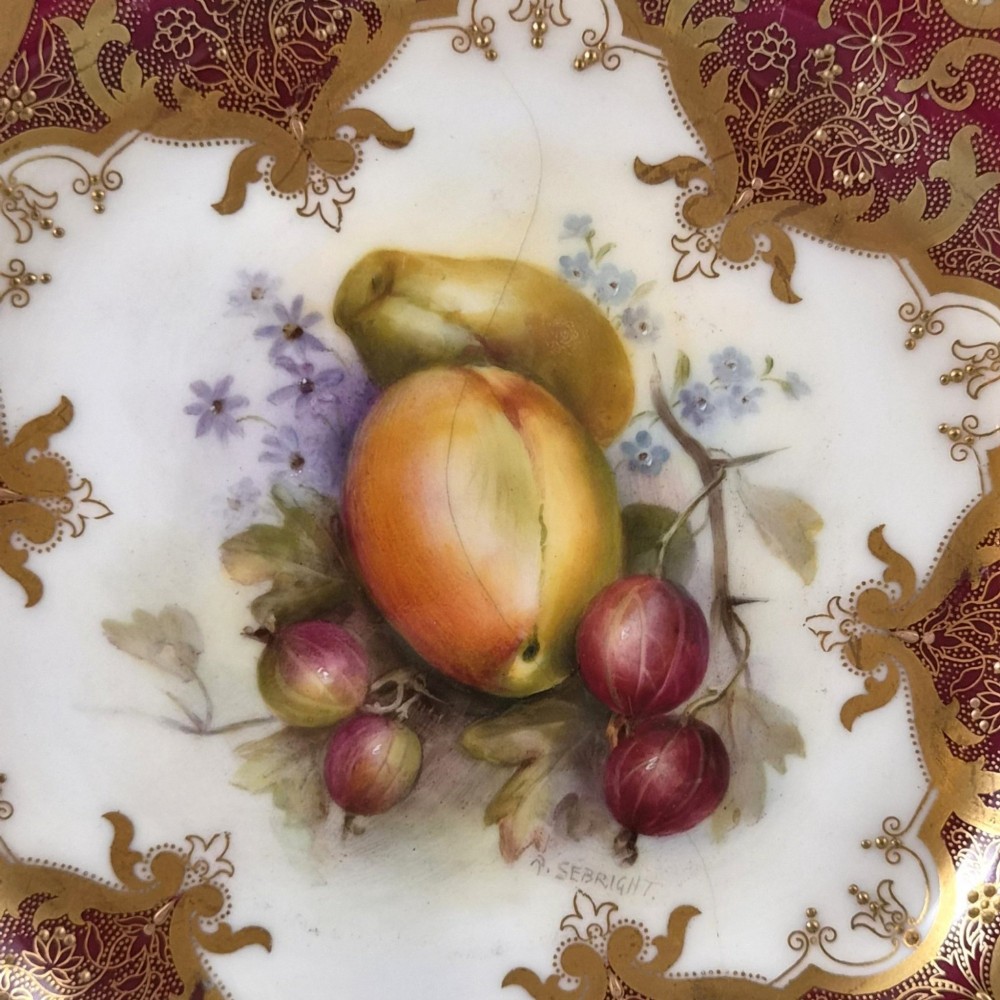 A circular porcelain cabinet plate featuring a central hand-painted fruit still life surrounded by a heavily gilded burgundy rim with scalloped edges. View II