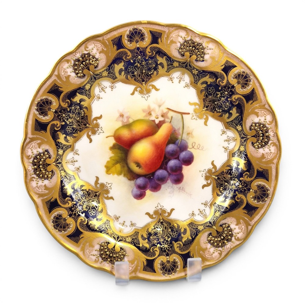 A circular porcelain cabinet plate featuring hand-painted pears and grapes in the centre, framed by an ornate cobalt blue and gold leaf scrollwork border.