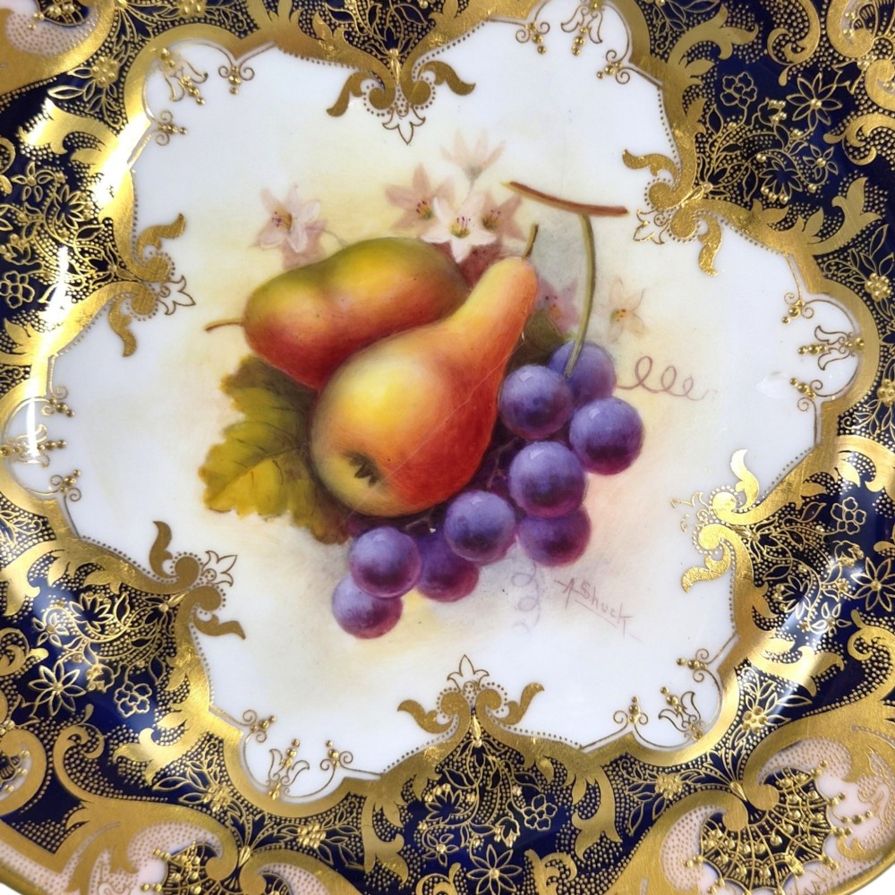A circular porcelain cabinet plate featuring hand-painted pears and grapes in the centre, framed by an ornate cobalt blue and gold leaf scrollwork border. View III