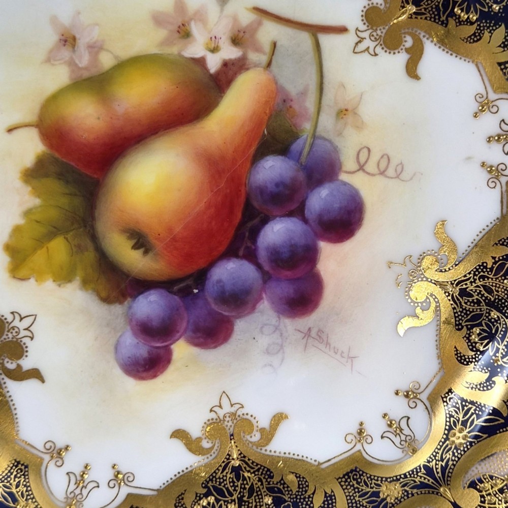 A circular porcelain cabinet plate featuring hand-painted pears and grapes in the centre, framed by an ornate cobalt blue and gold leaf scrollwork border. View IV