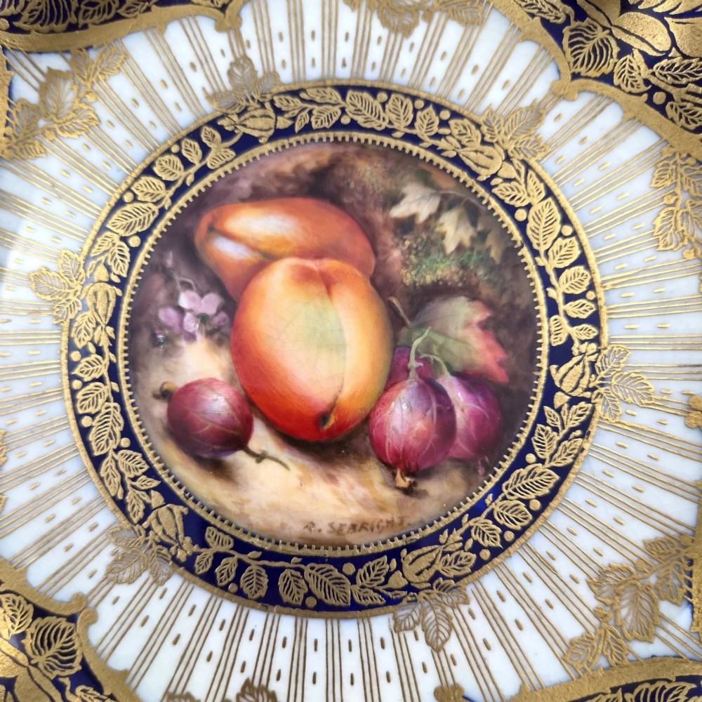 A circular porcelain cabinet plate featuring a central hand-painted fruit still life surrounded by a gilded sunburst pattern and a cobalt blue rim embellished with gold floral scrollwork. View II