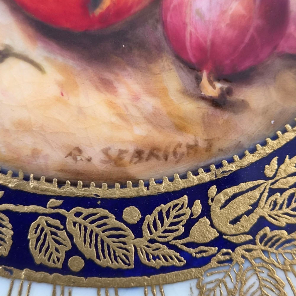 A circular porcelain cabinet plate featuring a central hand-painted fruit still life surrounded by a gilded sunburst pattern and a cobalt blue rim embellished with gold floral scrollwork. View III