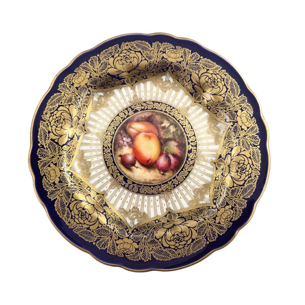 A circular porcelain cabinet plate featuring a central hand-painted fruit still life surrounded by a gilded sunburst pattern and a cobalt blue rim embellished with gold floral scrollwork. View XI
