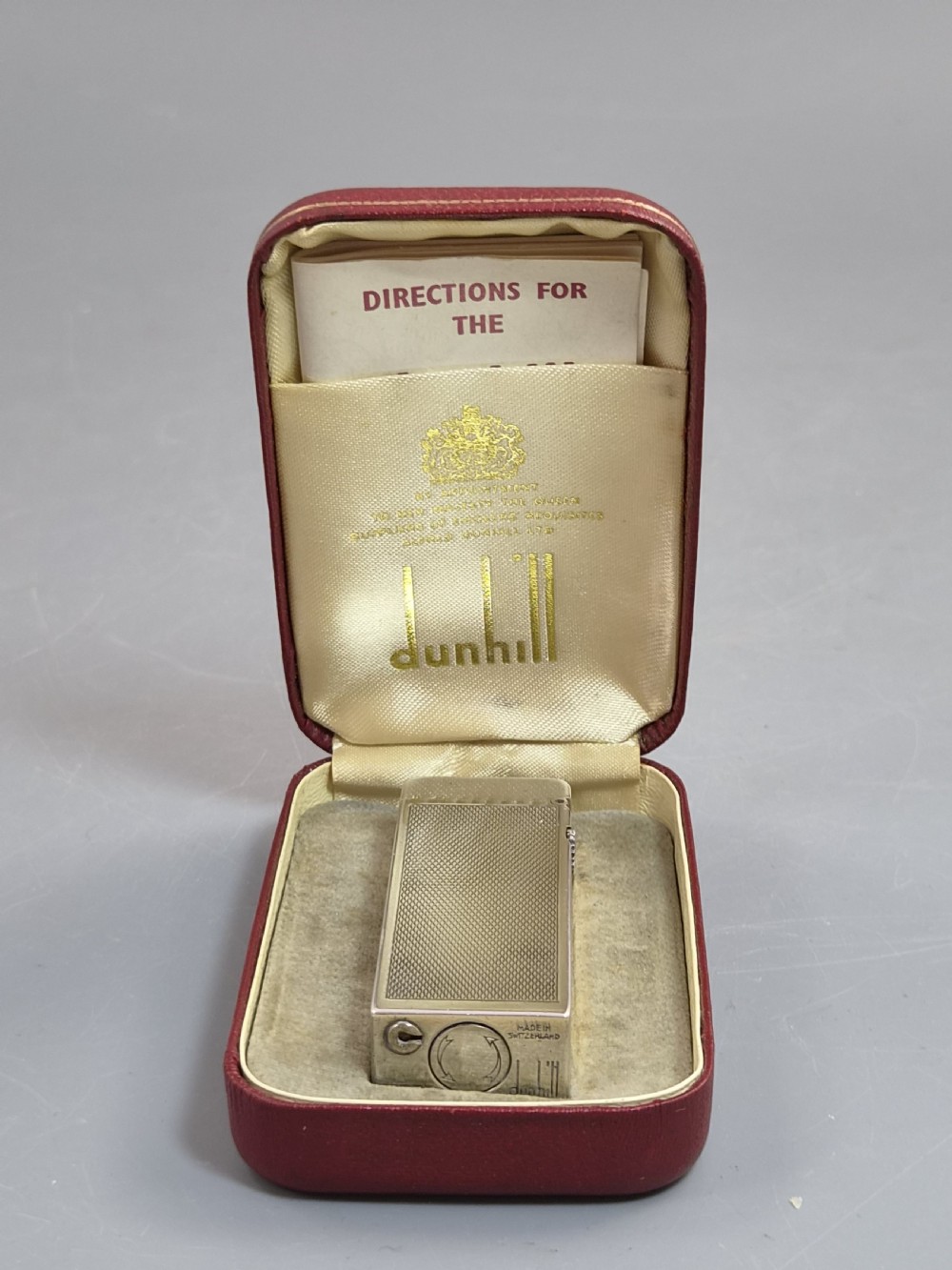 A silver-toned Dunhill Rollagas lighter shown alongside its original paper instruction booklet and red leatherette presentation case. View II