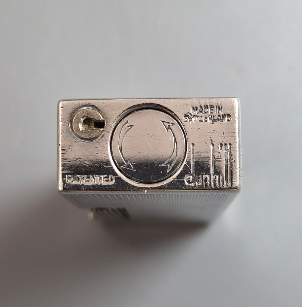 A silver-toned Dunhill Rollagas lighter shown alongside its original paper instruction booklet and red leatherette presentation case. View IX