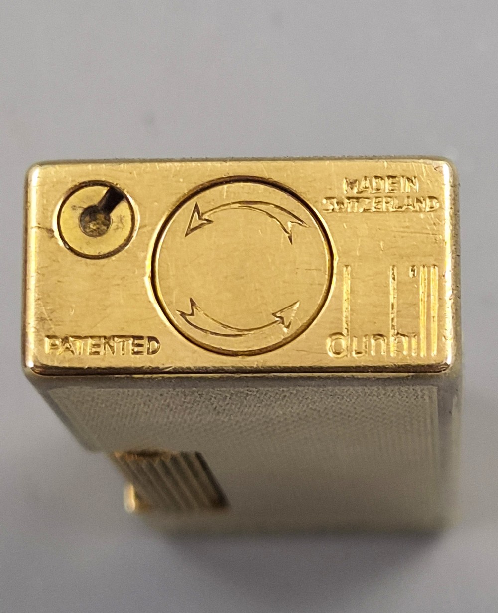 A 1967 gold-plated Dunhill Rollagas pocket lighter with a textured barley pattern, displayed alongside its fitted red presentation case and original printed instruction booklet. View VI