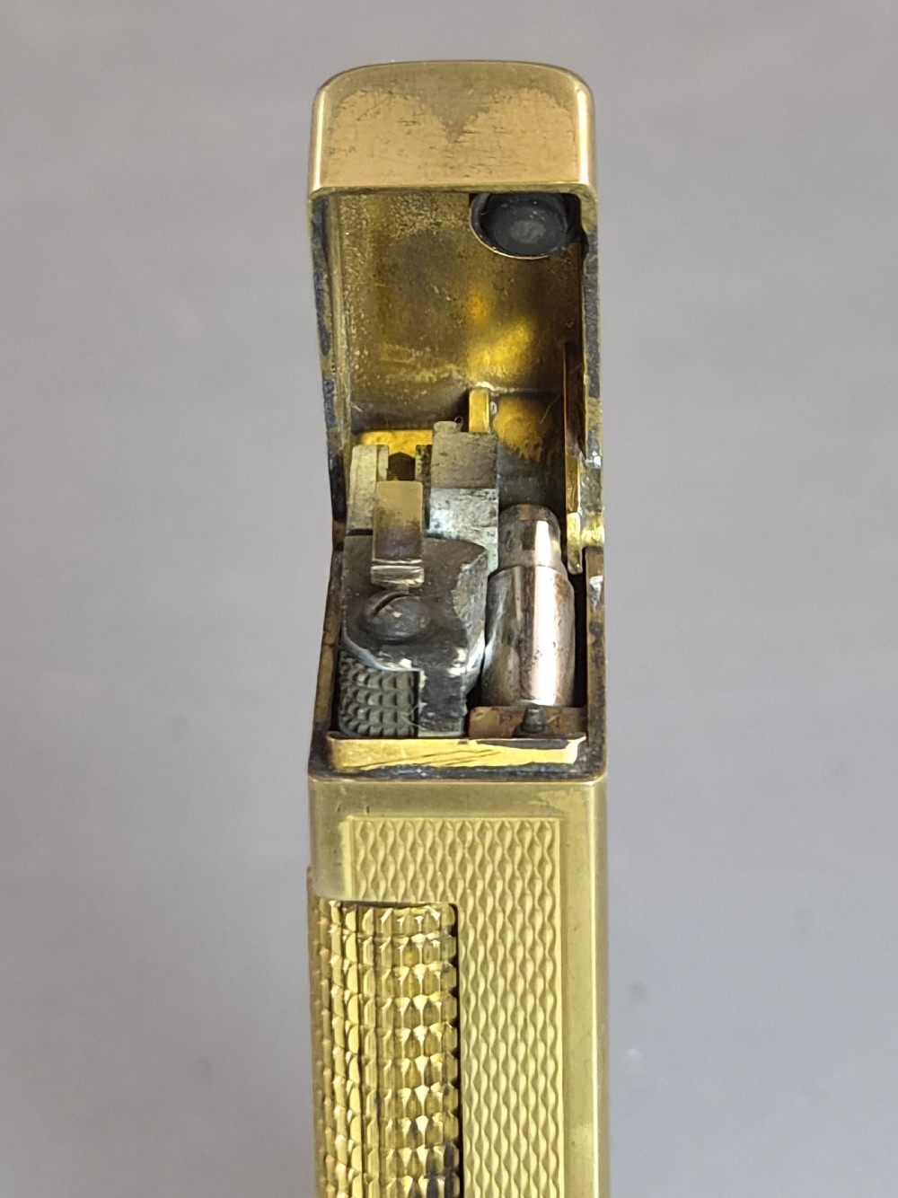 A 1967 gold-plated Dunhill Rollagas pocket lighter with a textured barley pattern, displayed alongside its fitted red presentation case and original printed instruction booklet. View VII