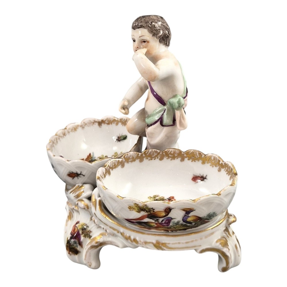 A 19th-century German hard-paste porcelain double salt cellar featuring a central sculpted figure of a cherub flanked by two shell-shaped bowls hand-painted with birds and insects. View II