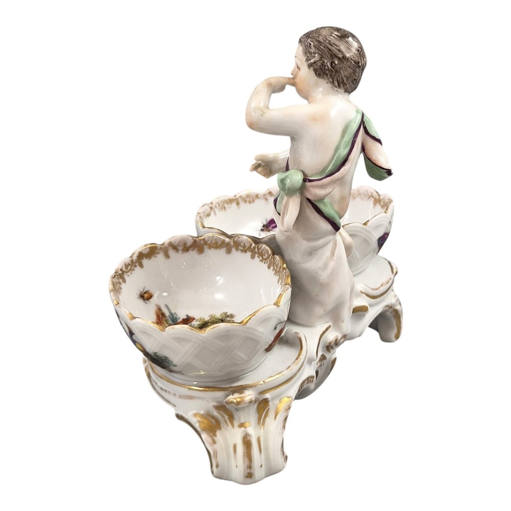 A 19th-century German hard-paste porcelain double salt cellar featuring a central sculpted figure of a cherub flanked by two shell-shaped bowls hand-painted with birds and insects. View III