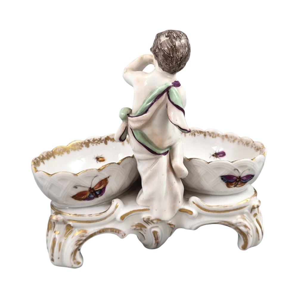 A 19th-century German hard-paste porcelain double salt cellar featuring a central sculpted figure of a cherub flanked by two shell-shaped bowls hand-painted with birds and insects. View IV