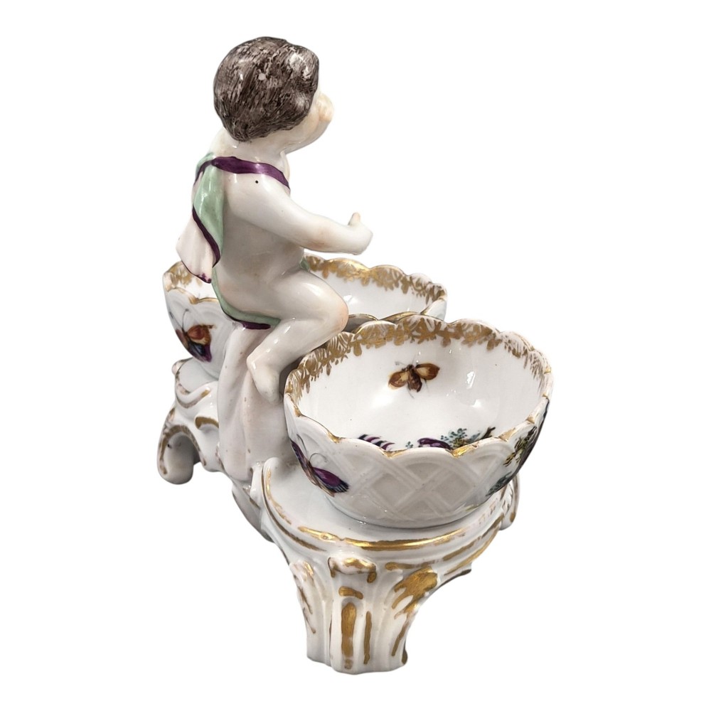 A 19th-century German hard-paste porcelain double salt cellar featuring a central sculpted figure of a cherub flanked by two shell-shaped bowls hand-painted with birds and insects. View V