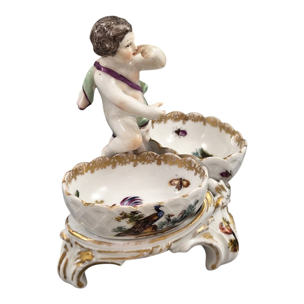 A 19th-century German hard-paste porcelain double salt cellar featuring a central sculpted figure of a cherub flanked by two shell-shaped bowls hand-painted with birds and insects. View VI