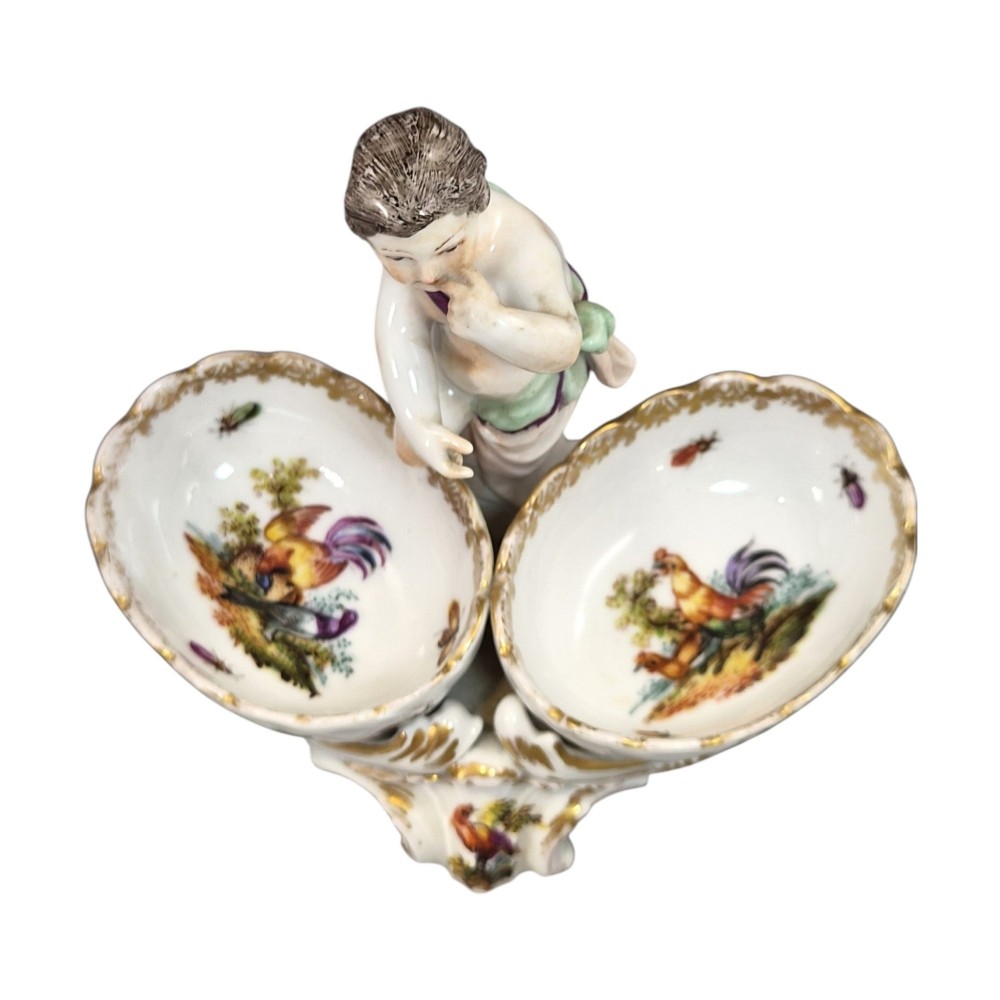 A 19th-century German hard-paste porcelain double salt cellar featuring a central sculpted figure of a cherub flanked by two shell-shaped bowls hand-painted with birds and insects. View VII