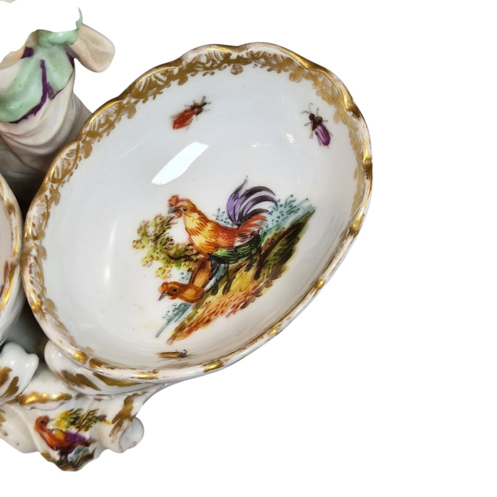 A 19th-century German hard-paste porcelain double salt cellar featuring a central sculpted figure of a cherub flanked by two shell-shaped bowls hand-painted with birds and insects. View VIII