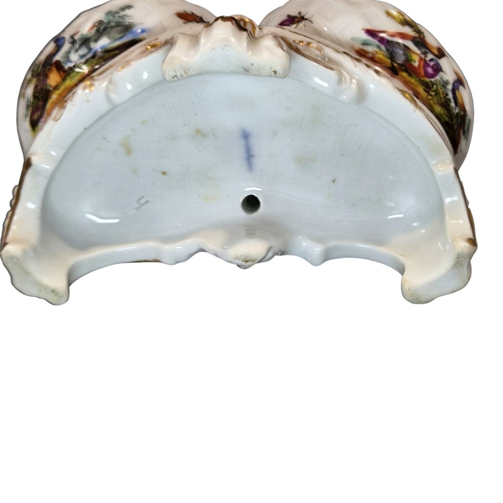 A 19th-century German hard-paste porcelain double salt cellar featuring a central sculpted figure of a cherub flanked by two shell-shaped bowls hand-painted with birds and insects. View XII