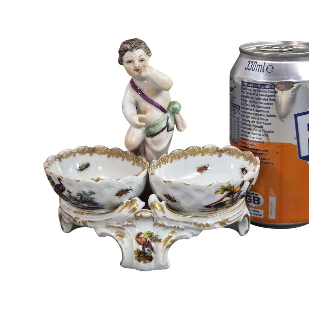 A 19th-century German hard-paste porcelain double salt cellar featuring a central sculpted figure of a cherub flanked by two shell-shaped bowls hand-painted with birds and insects. View XIII