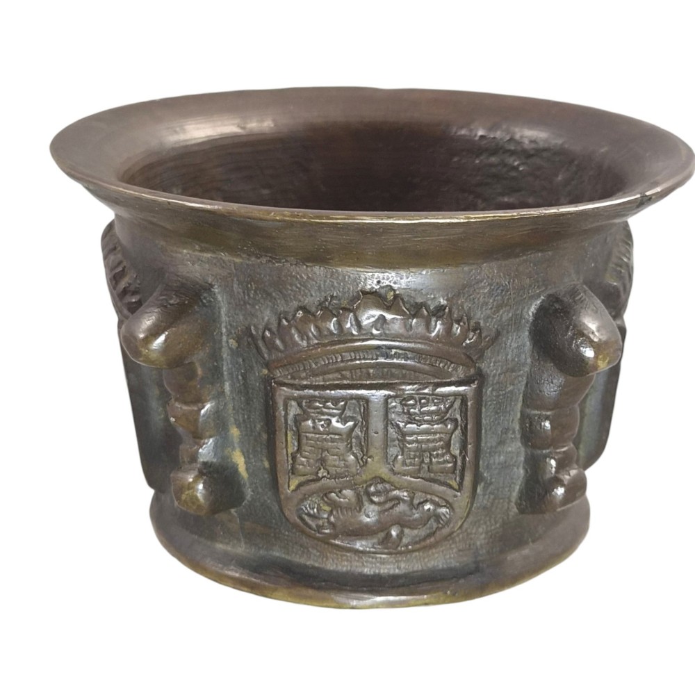 A heavy 17th-century cast bronze apothecary mortar featuring raised heraldic coat of arms motifs and side lugs around a flared rim. View II