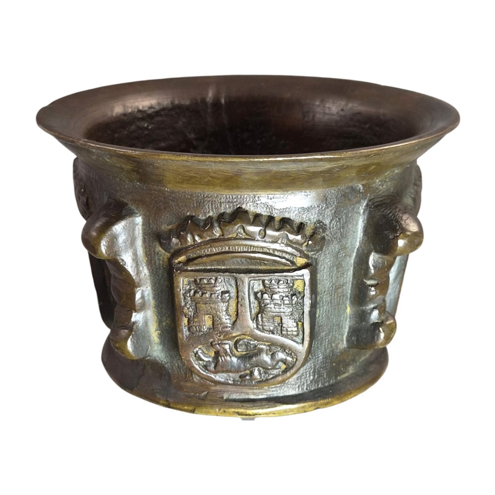 A heavy 17th-century cast bronze apothecary mortar featuring raised heraldic coat of arms motifs and side lugs around a flared rim. View IX