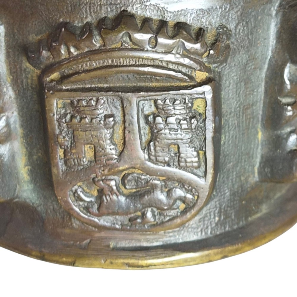 A heavy 17th-century cast bronze apothecary mortar featuring raised heraldic coat of arms motifs and side lugs around a flared rim. View X