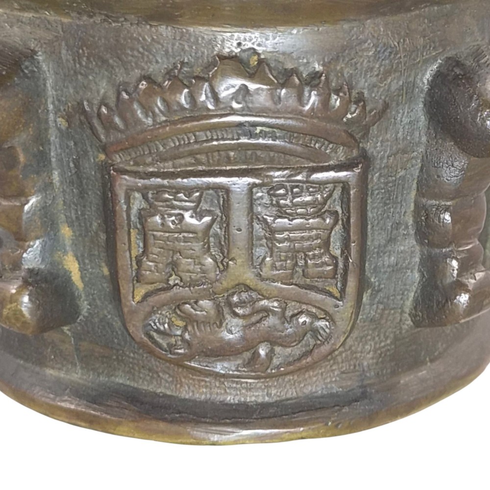 A heavy 17th-century cast bronze apothecary mortar featuring raised heraldic coat of arms motifs and side lugs around a flared rim. View XII