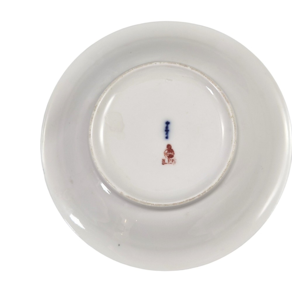 An antique white and gilt porcelain presentation cup with an elevated loop handle sitting on a matching gilded saucer. View IV