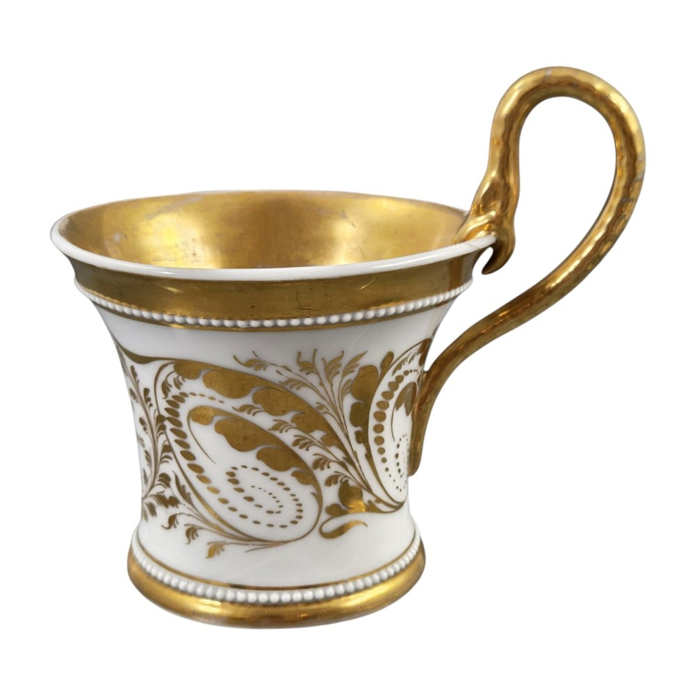 An antique white and gilt porcelain presentation cup with an elevated loop handle sitting on a matching gilded saucer. View VI