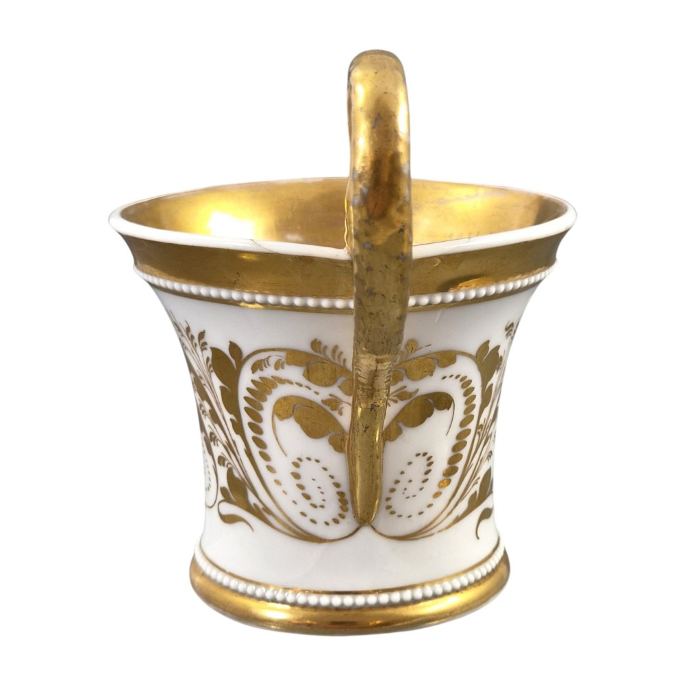 An antique white and gilt porcelain presentation cup with an elevated loop handle sitting on a matching gilded saucer. View VII
